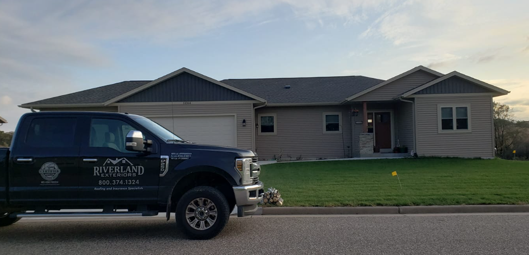 Dark truck parked in front of a house. The house has a garage and a front porch.