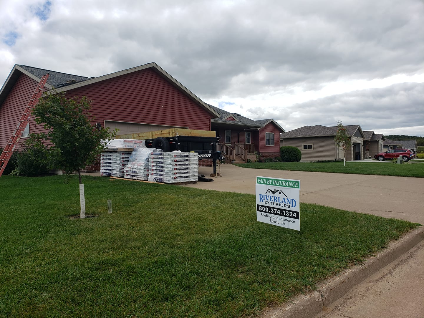 Houses with roofing materials and a sign on the lawn. Cloudy sky, green grass, street.