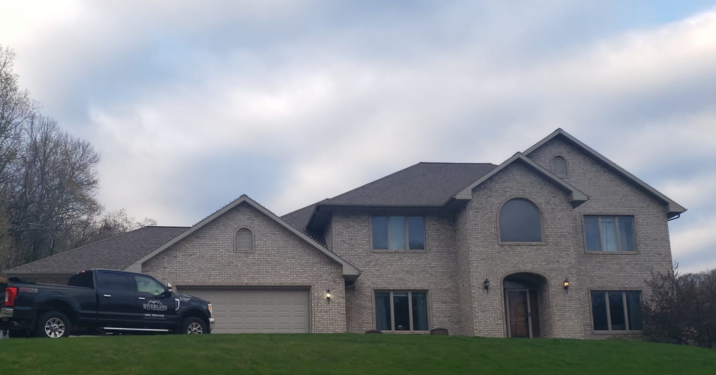 A two-story brick house with a dark roof and a black truck parked on the lawn.