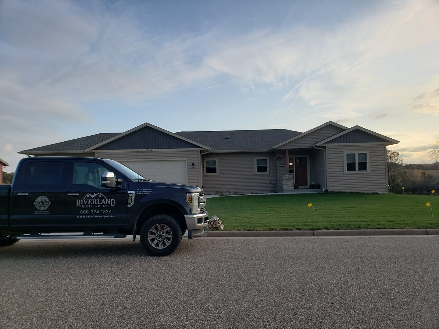 Dark blue truck parked in front of a tan house with a green lawn. Cloudy sky in the background.