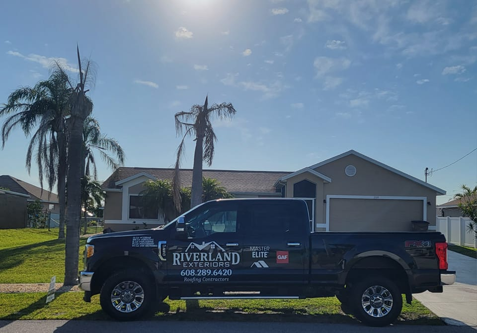 Black truck parked in front of a house on a sunny day. The truck has a logo for Riverland Exteriors.