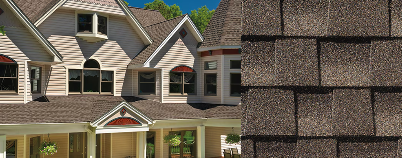 A house with brown shingle roof. Close up of roof shingles on the right. Blue sky is visible.