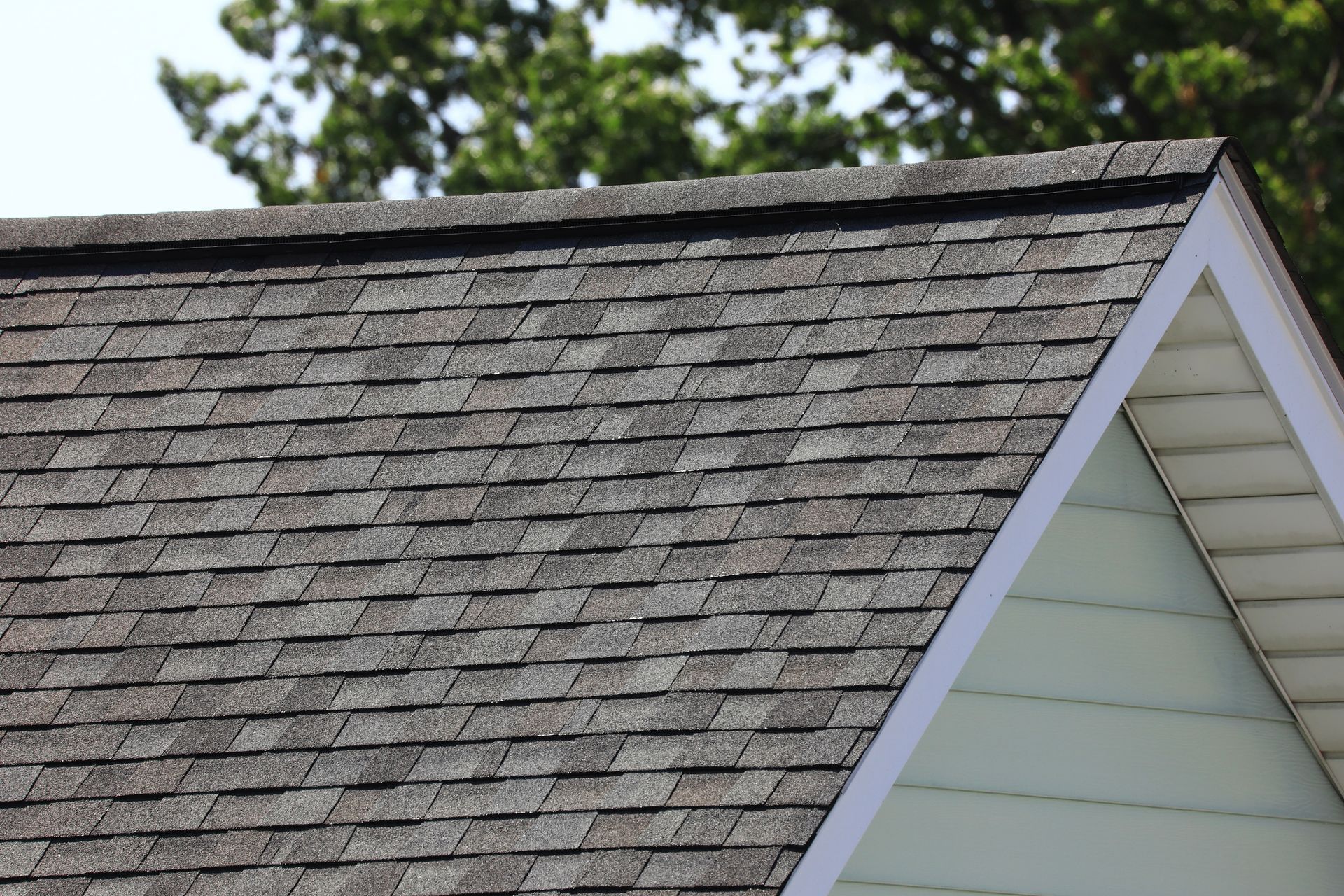 Close-up view of a house roof with dark asphalt shingles under clear daylight.