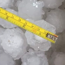 A yellow tape measure is sitting on top of a pile of hail.