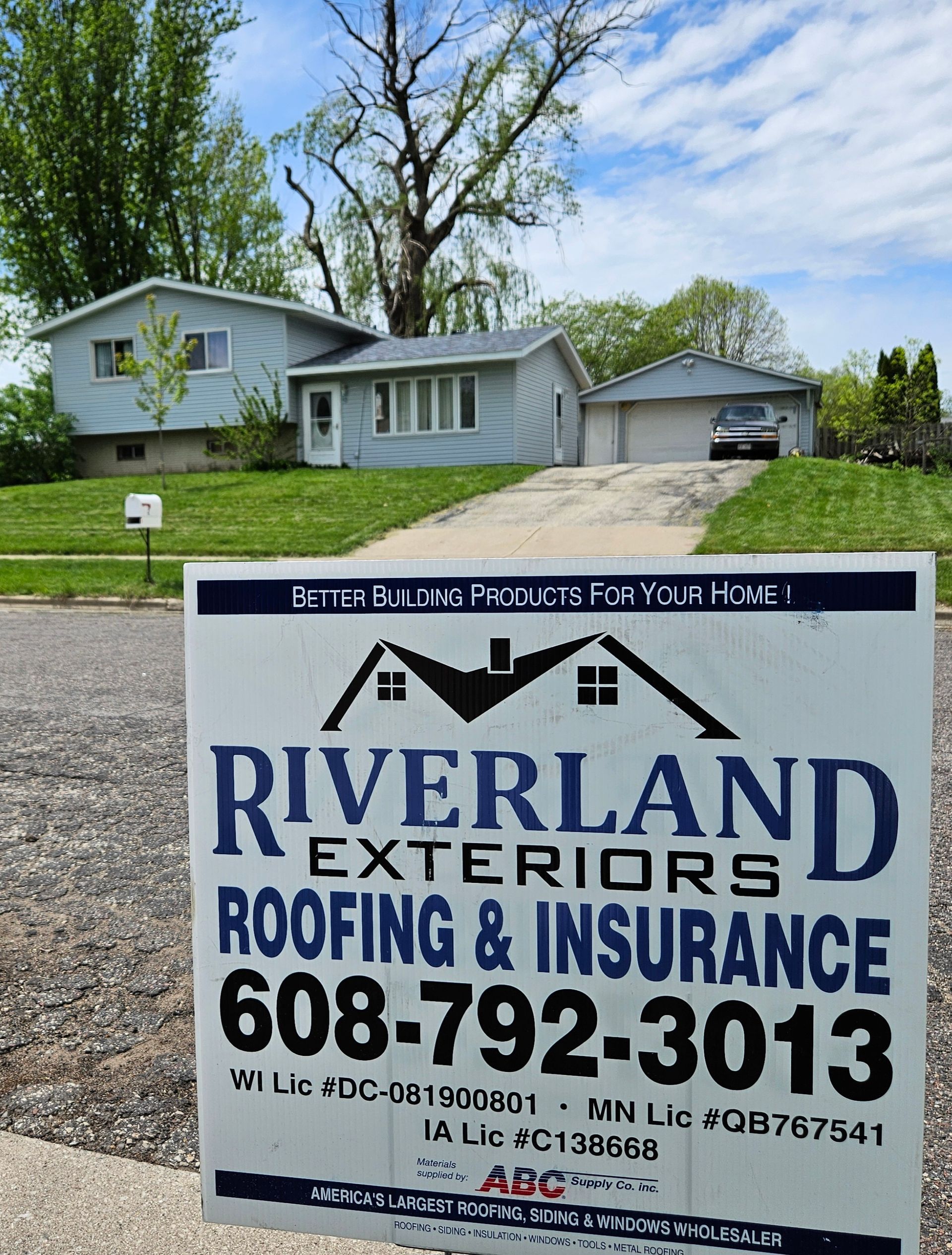 Sign for Riverland Exteriors roofing company in front of a gray house and garage.