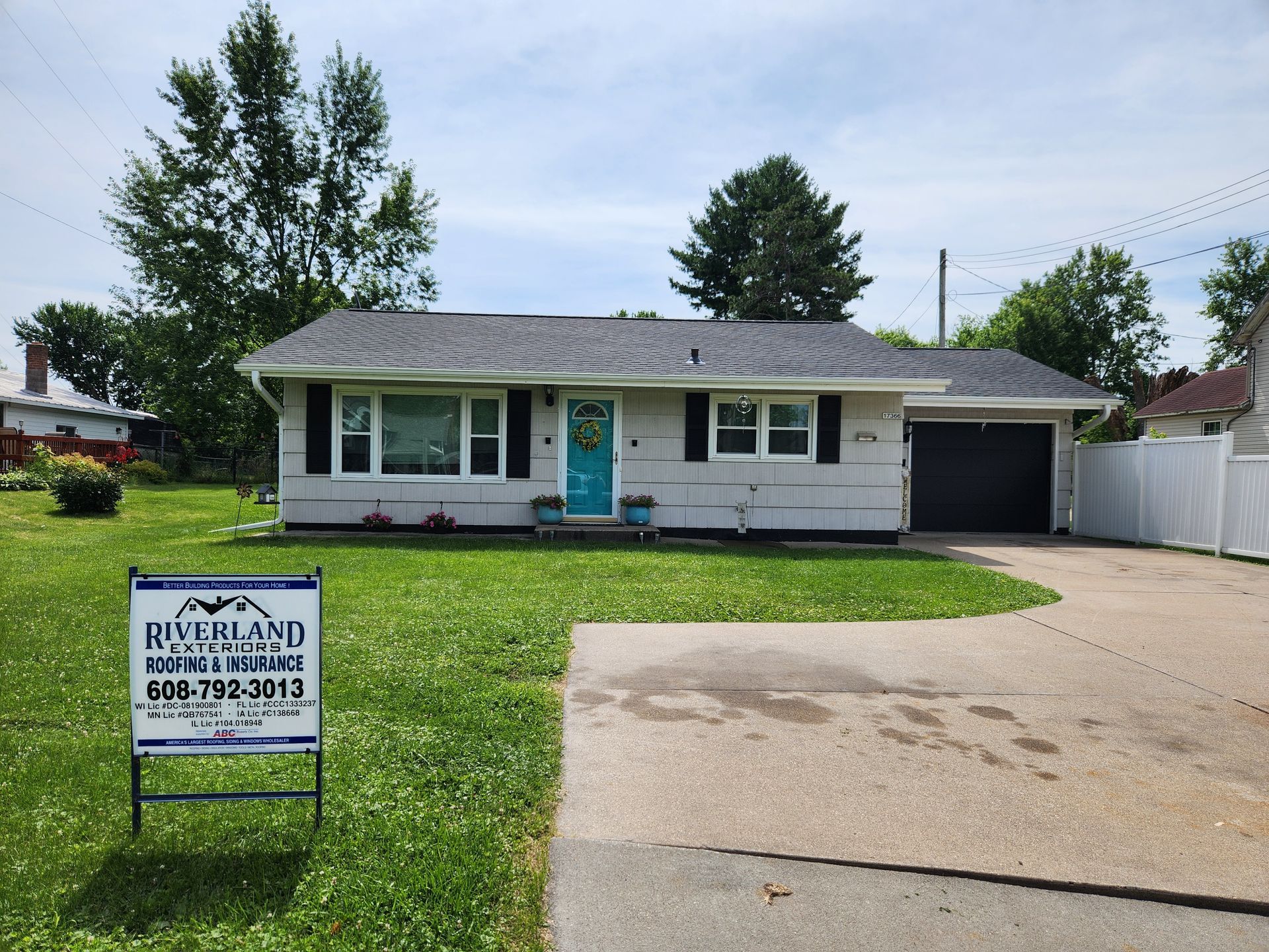 White ranch-style house with blue door, dark gray roof, and green lawn. A 