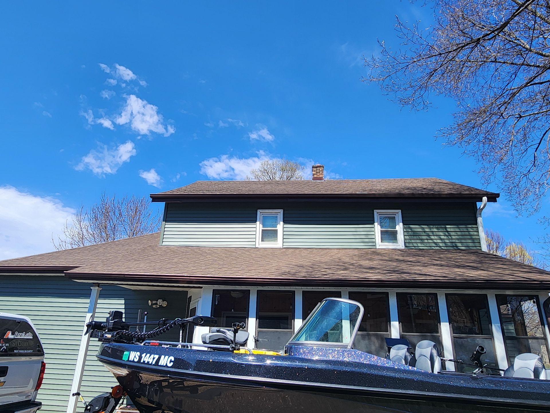 Boat parked in front of a green two-story house with a brown roof under a bright blue sky.