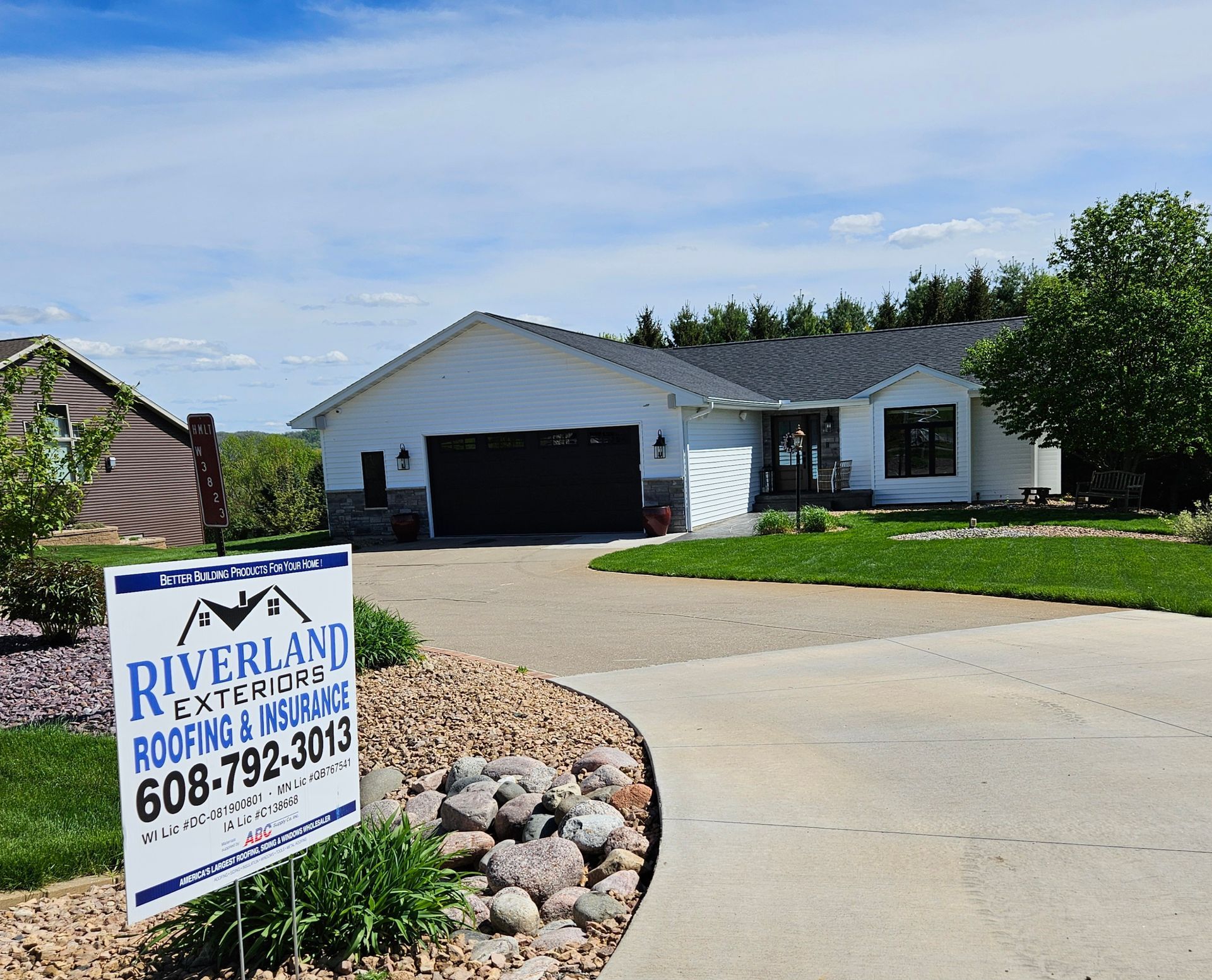 A white house with a dark garage door, sign for Riverland Exteriors in front.