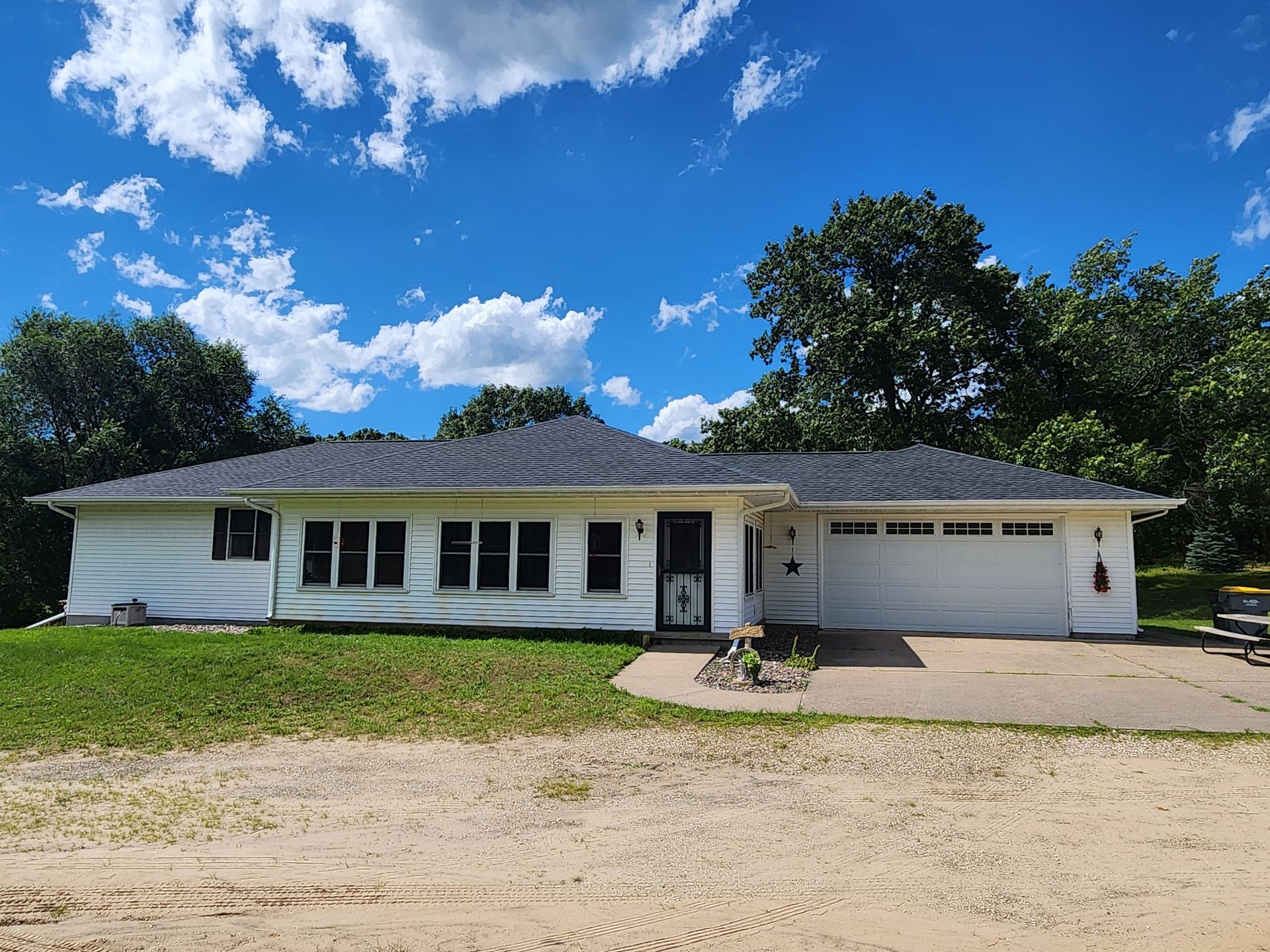 White ranch-style house with dark roof and garage door, set against a blue sky with clouds.