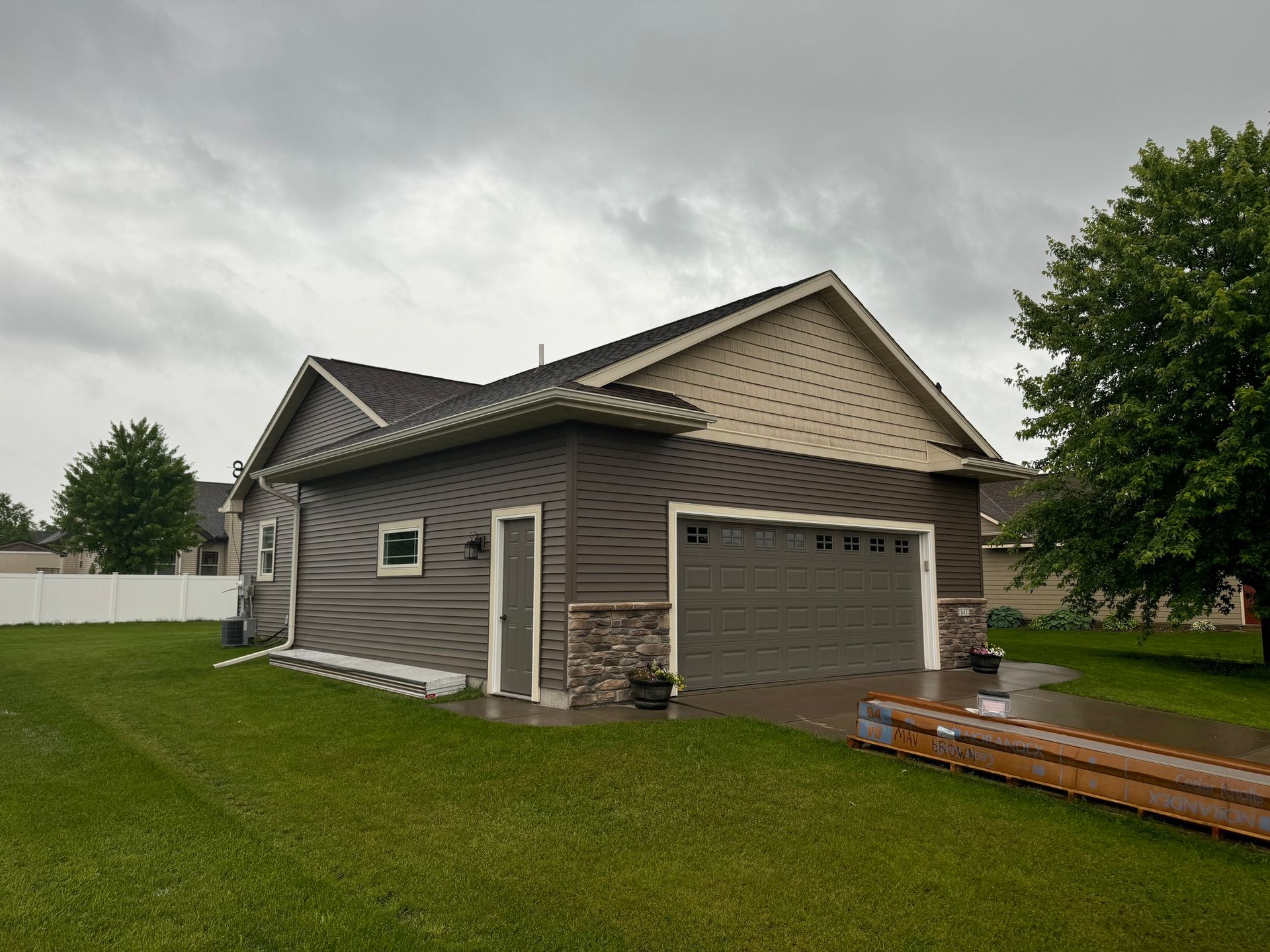 A brown and tan garage with a gray door and garage door on a grassy lawn under a cloudy sky.