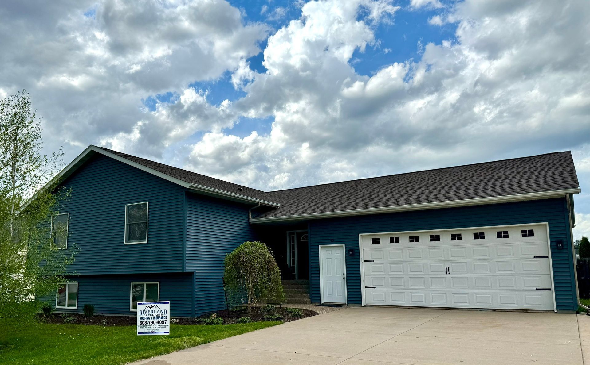 Blue house with a white garage door against a cloudy sky.