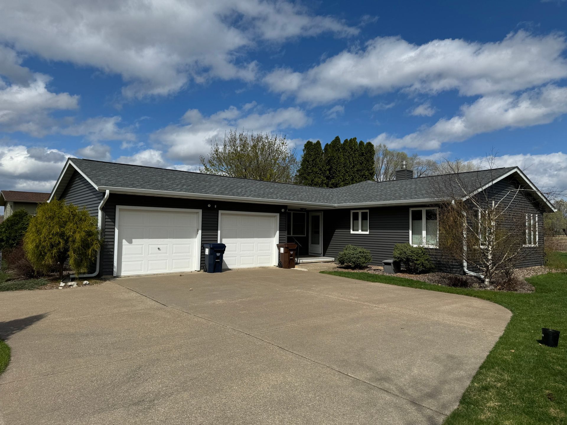 Single-story suburban house with attached garage, gravel driveway, and partly cloudy sky