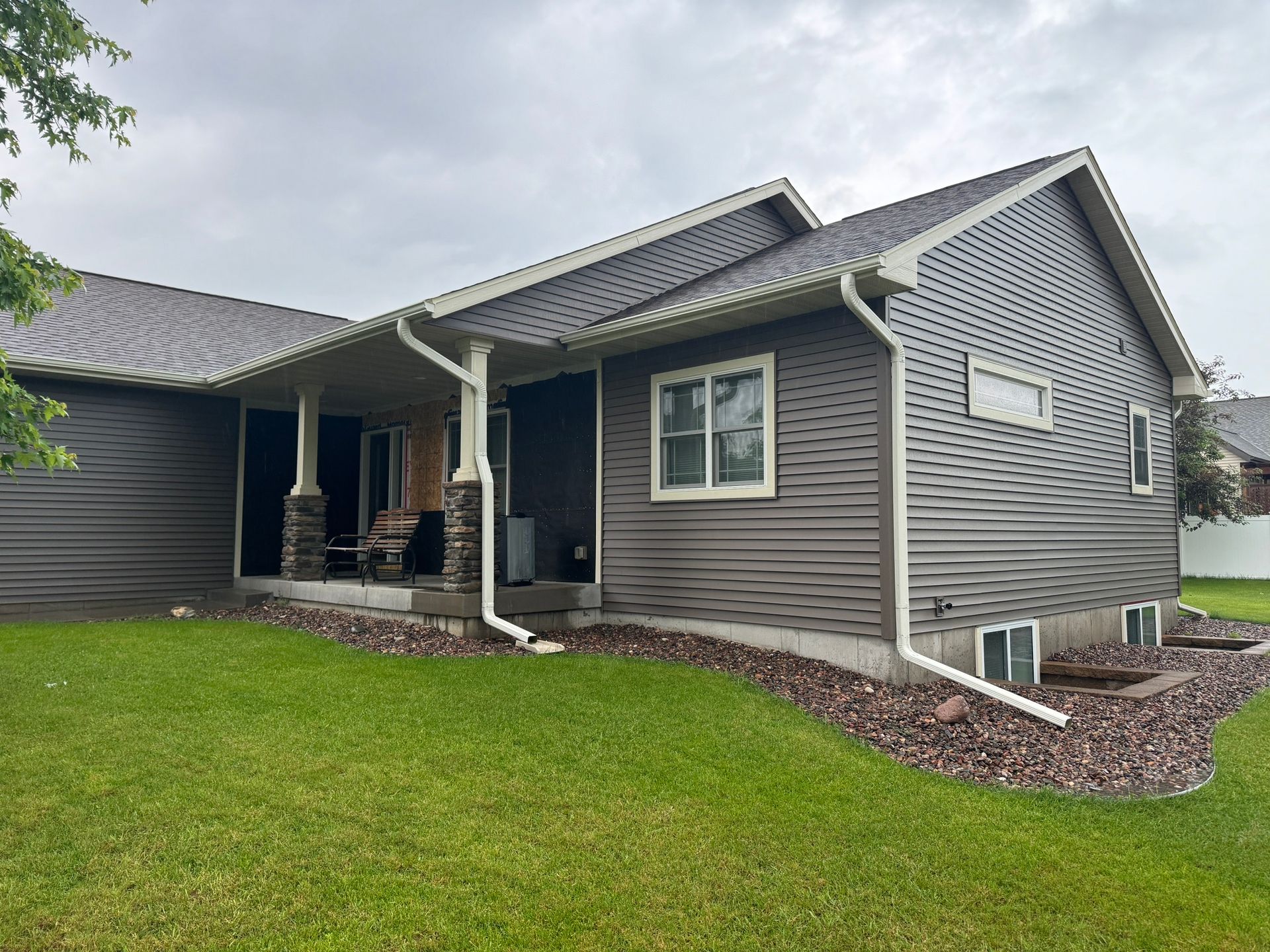 Gray house with white trim, porch, and green lawn. Cloudy sky overhead.