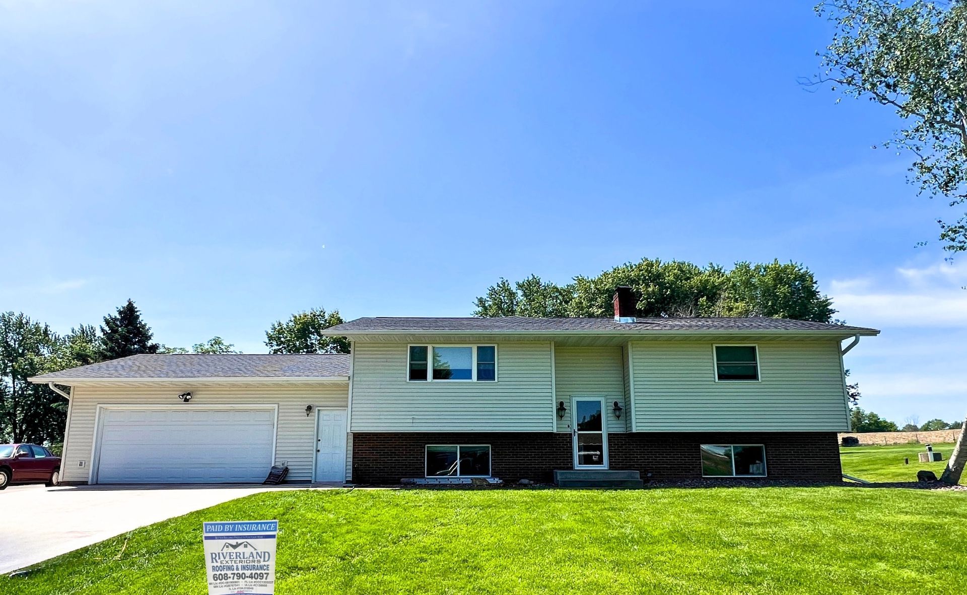 Two-story beige house with attached garage, green lawn, and blue sky.