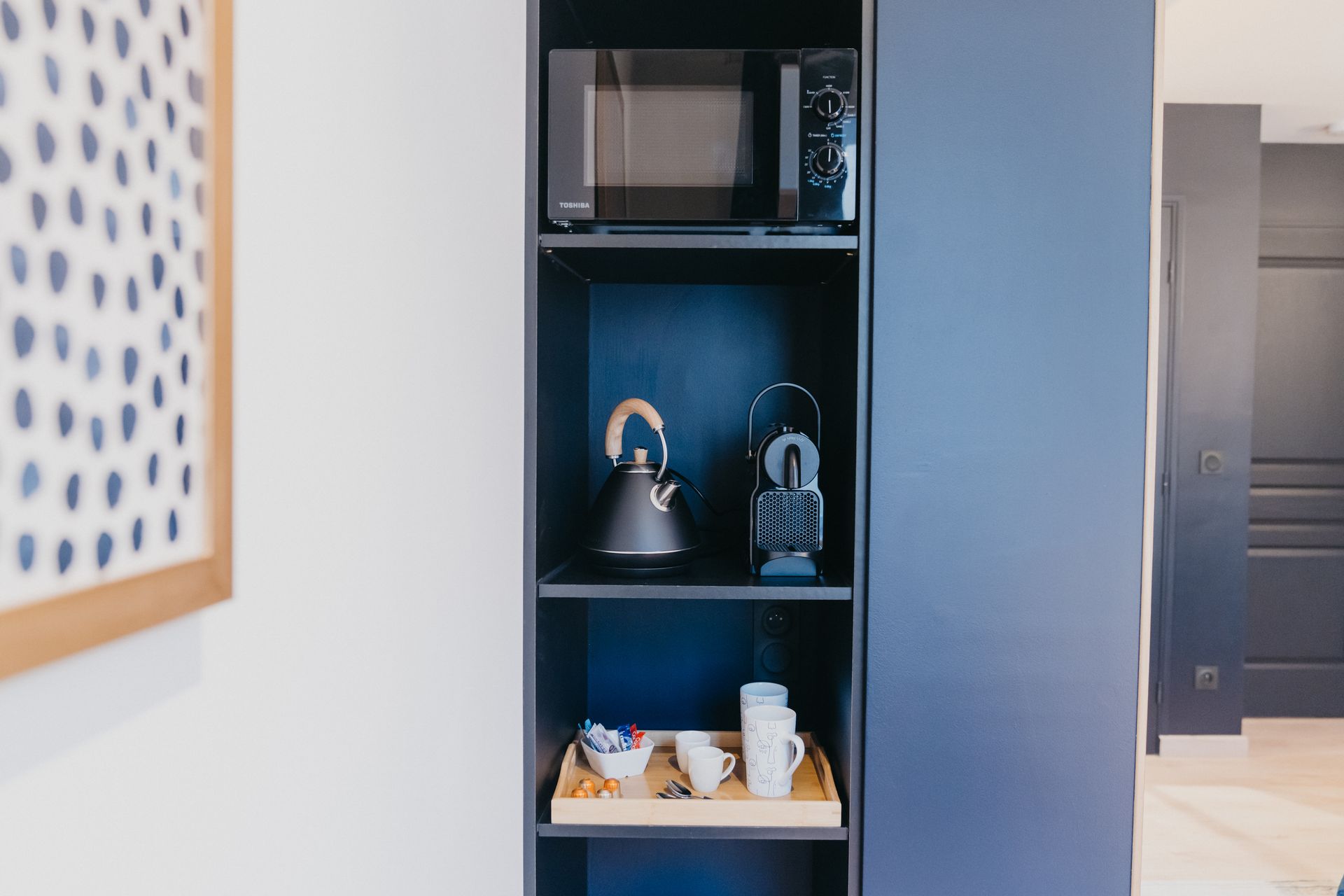 Une étagère bleue avec un micro-ondes et une bouilloire dessus.
