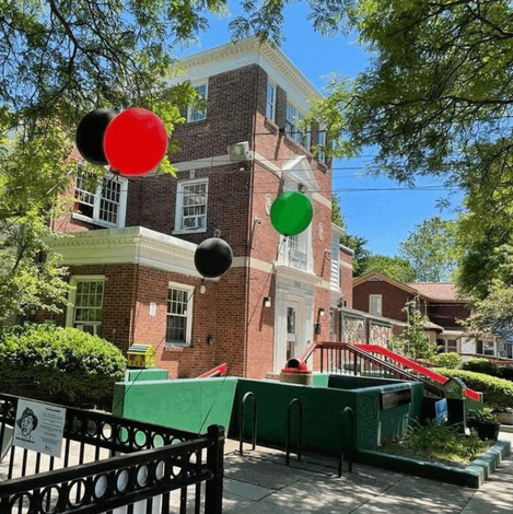 A brick building with balloons hanging from the trees in front of it