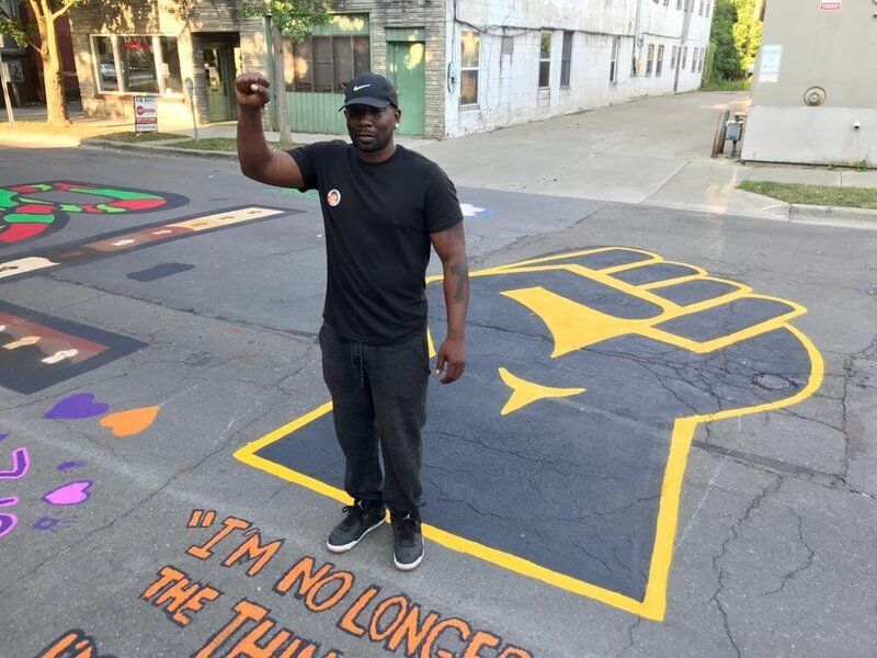 A man in a black shirt is standing in front of a drawing of a brain on the side of the road