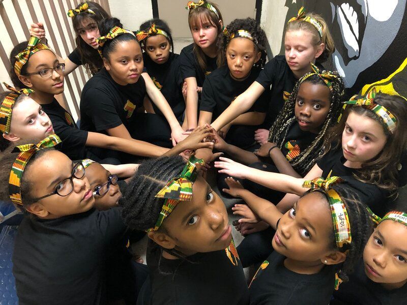 A group of young girls are putting their hands together in a circle.