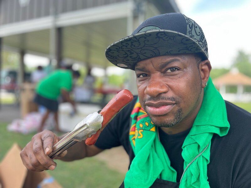 A man with a green scarf around his neck is holding a hot dog
