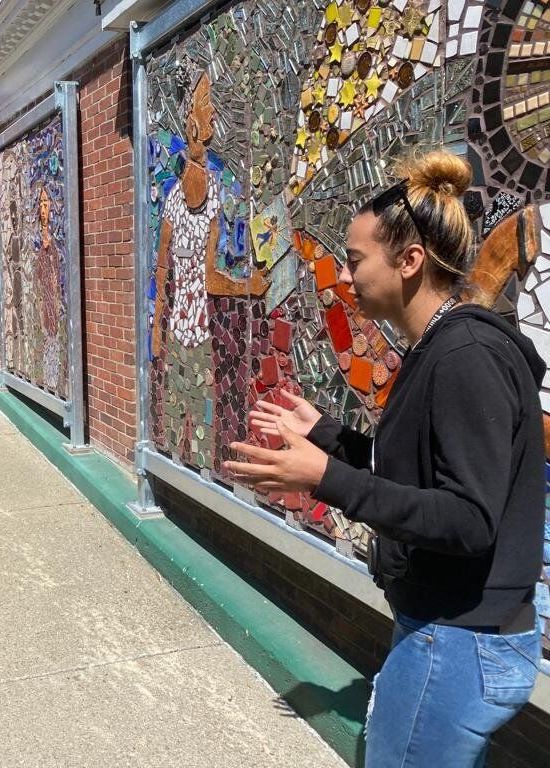 A woman is standing in front of a mosaic wall.