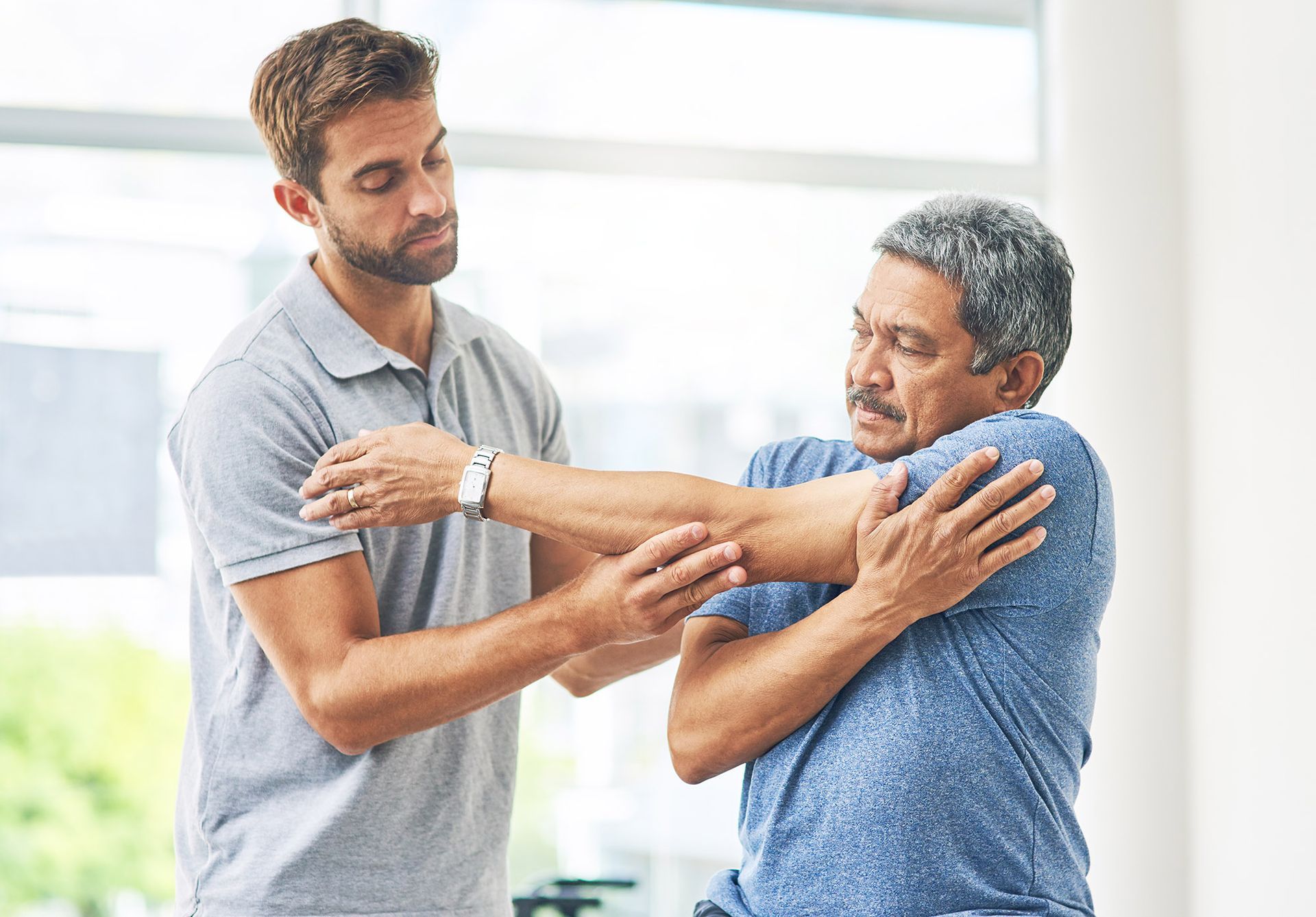 Physical therapist stretches patient's arm indoors.