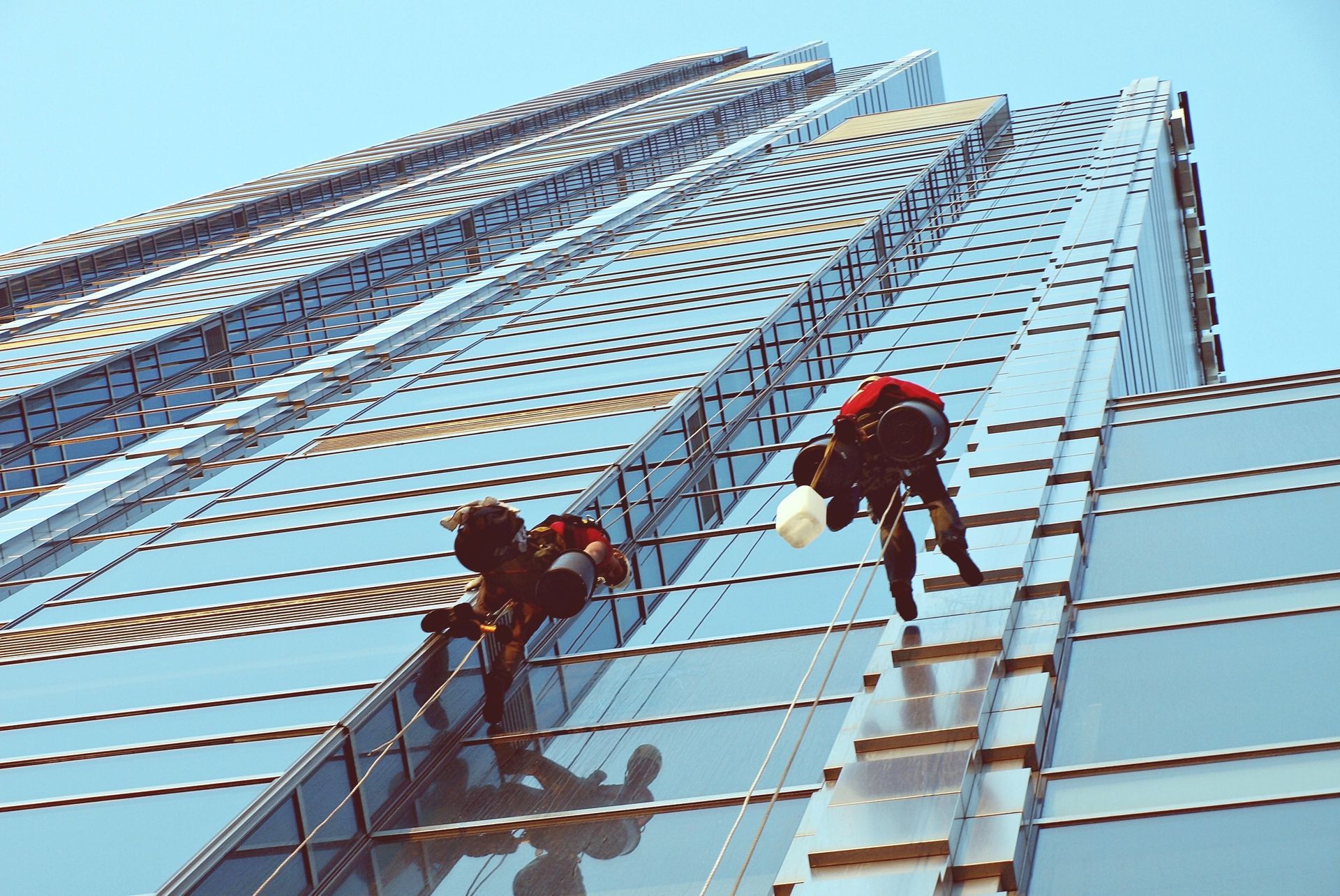 Person on a lift washes windows on a bright red building, blue sky in the background.