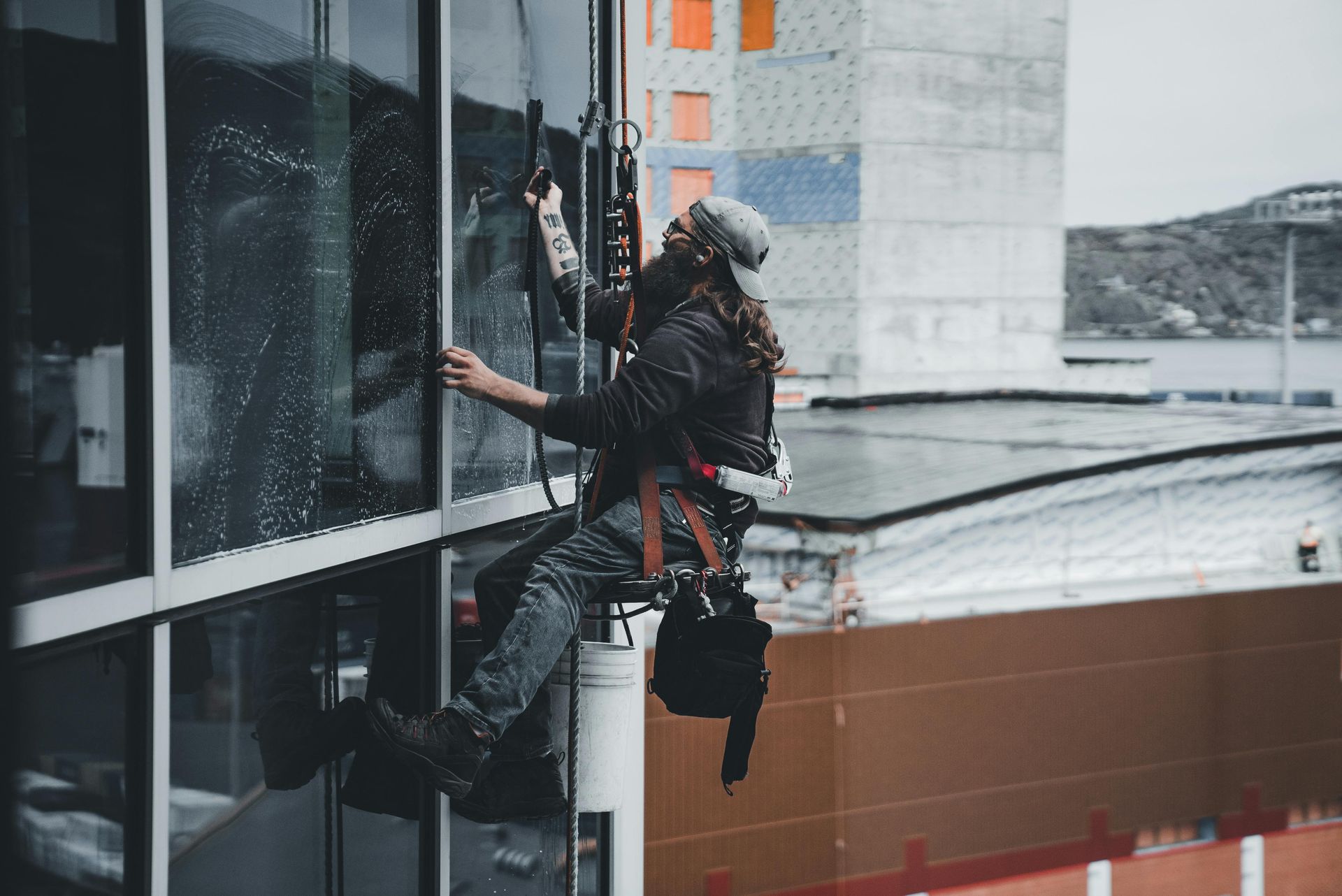 Six window washers in red shirts and hard hats cleaning the exterior of a glass high-rise building.