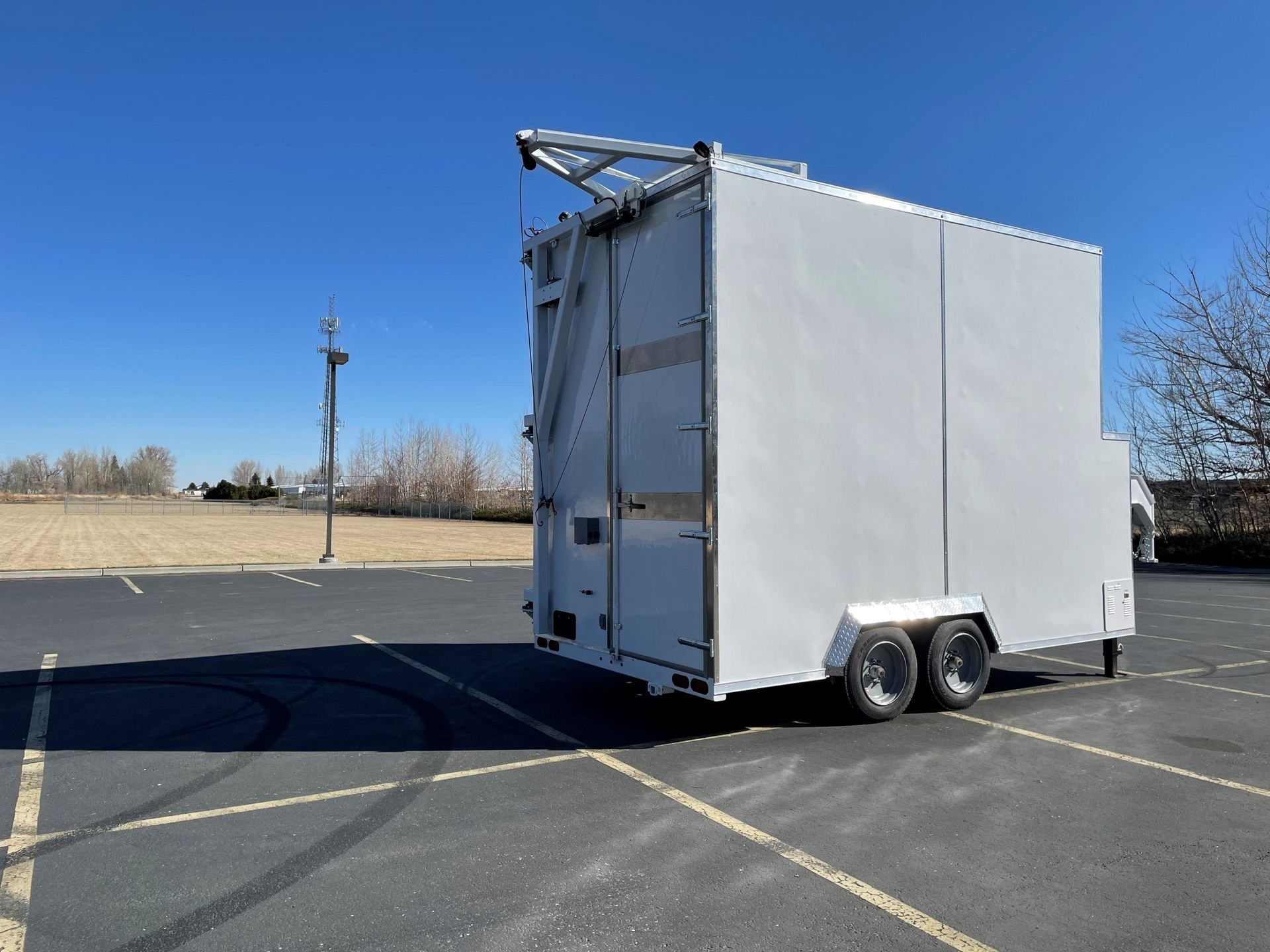 White enclosed butchering trailer for sale with rear ramp door parked on an empty paved lot under a clear blue sky