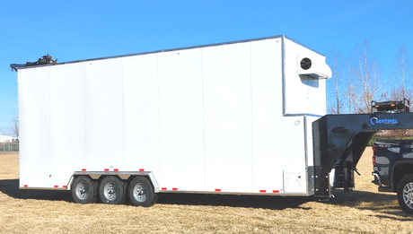 White enclosed refrigerated trailer hitched to a tan pickup in a parking lot at sunset