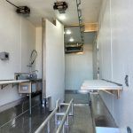 Narrow white galley kitchen with sink, cabinets, counter, and a small built-in table bench