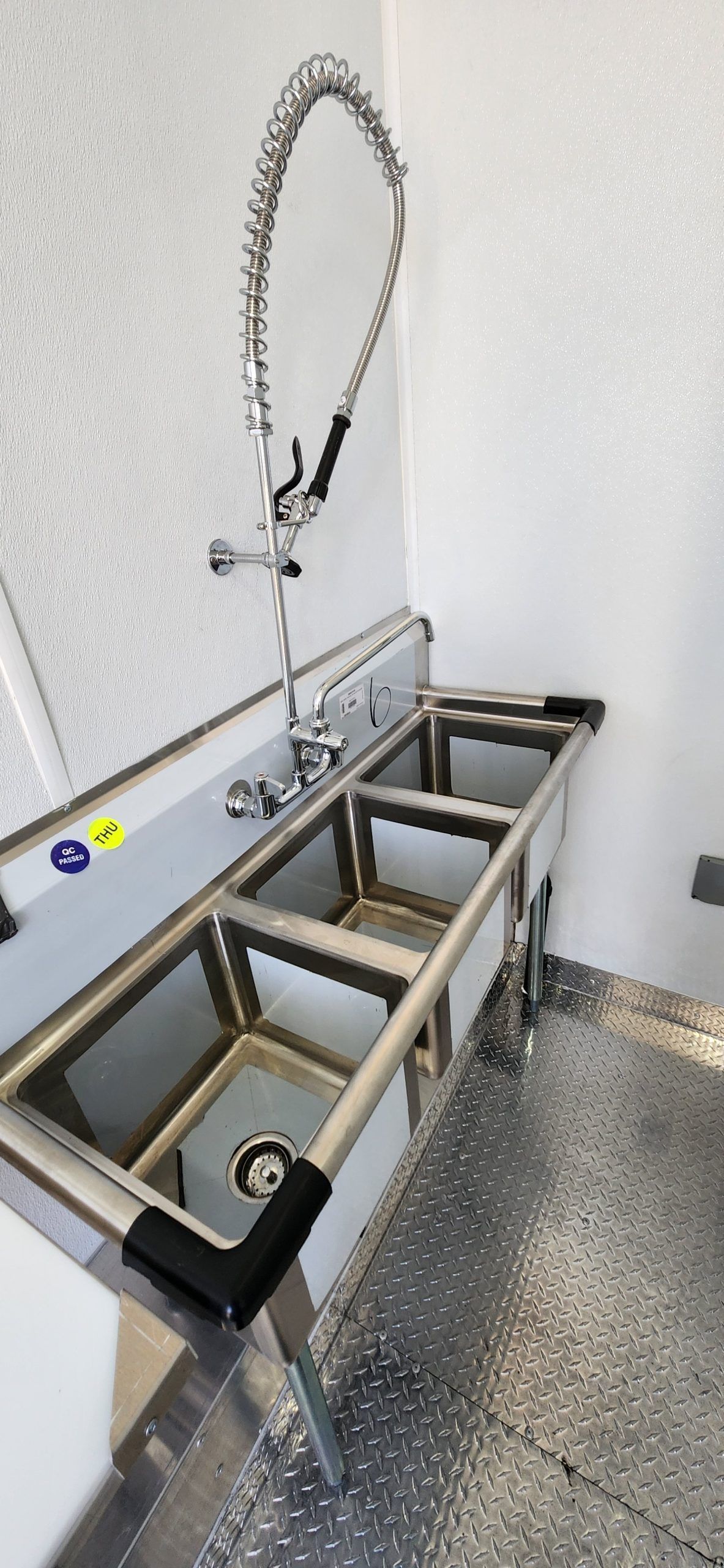 Stainless steel industrial sink station with a flexible hose and three framed compartments in a clean room.