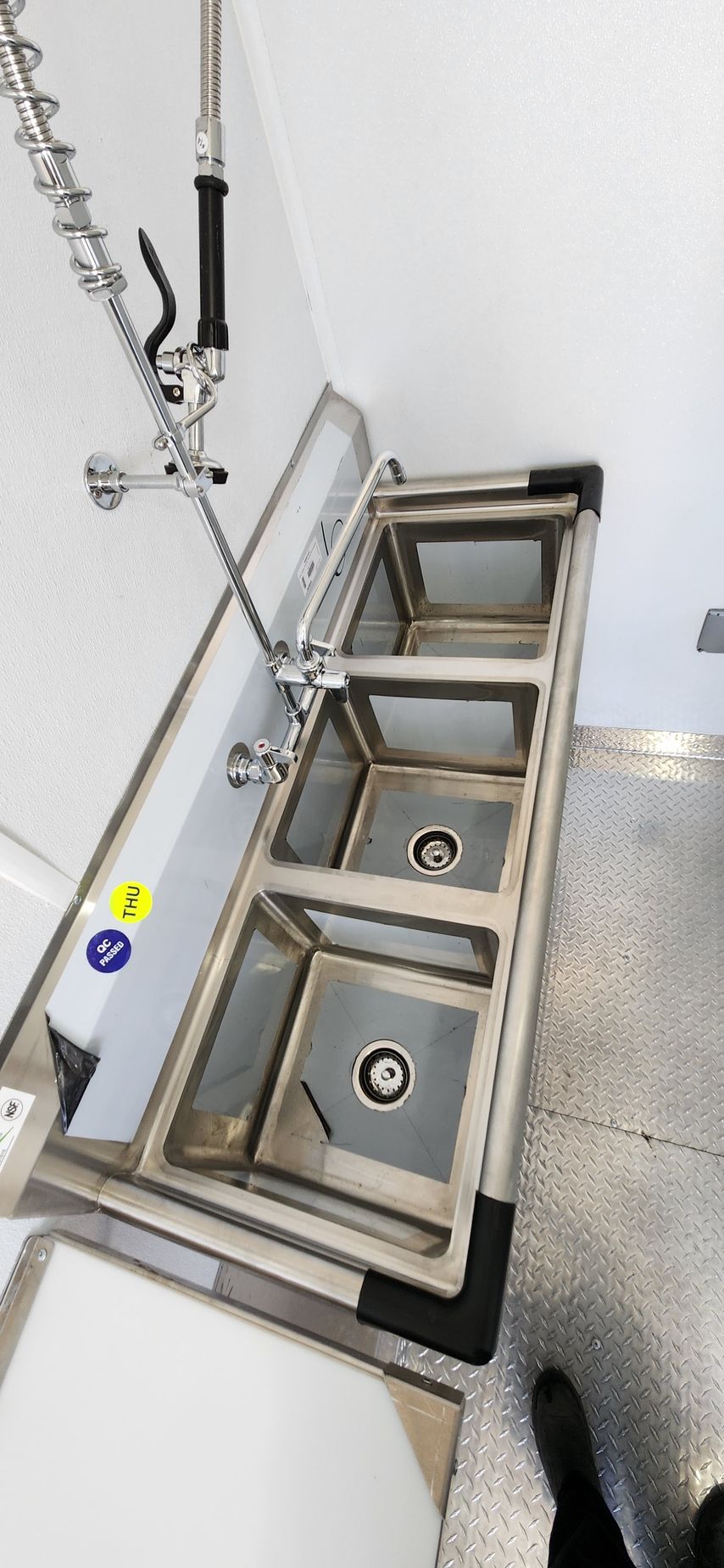 Stainless steel four-basin kitchen sink with faucet and drain baskets against a white wall.