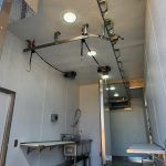Narrow interior room with high ceiling, track lights, sink, and staircase leading to a loft.
