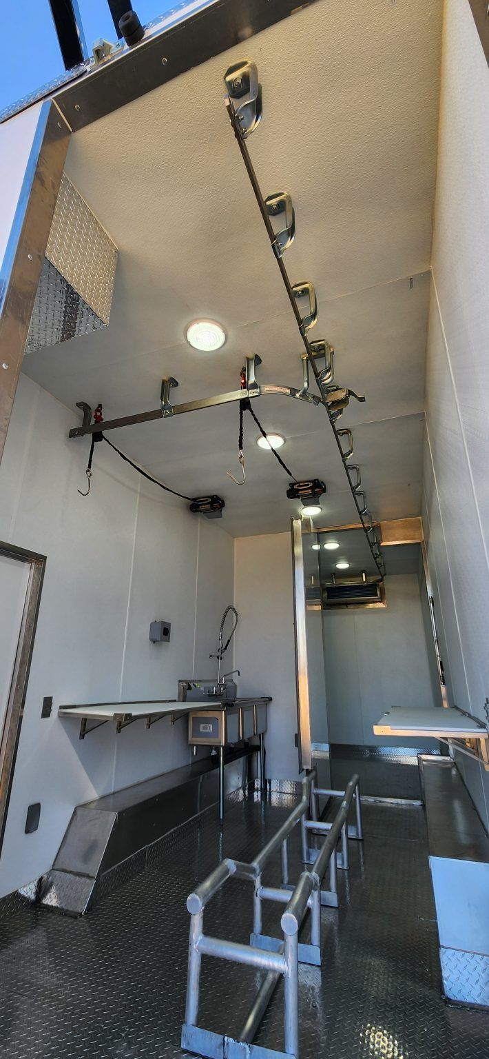 Mobile slaughter trailer with metal bar stools, counter, and ceiling track lights and hangers