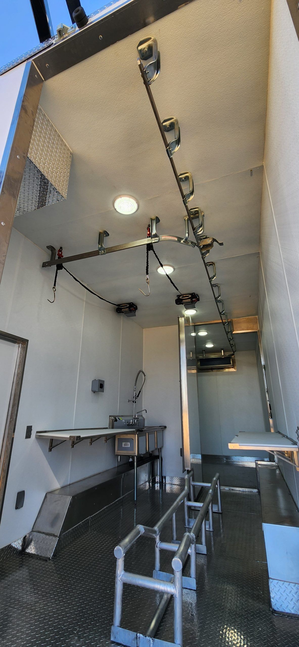 Narrow industrial room with metal equipment, overhead lights, and benches along the walls