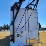 Black industrial machine mounted on a white trailer in a snowy field under a blue sky