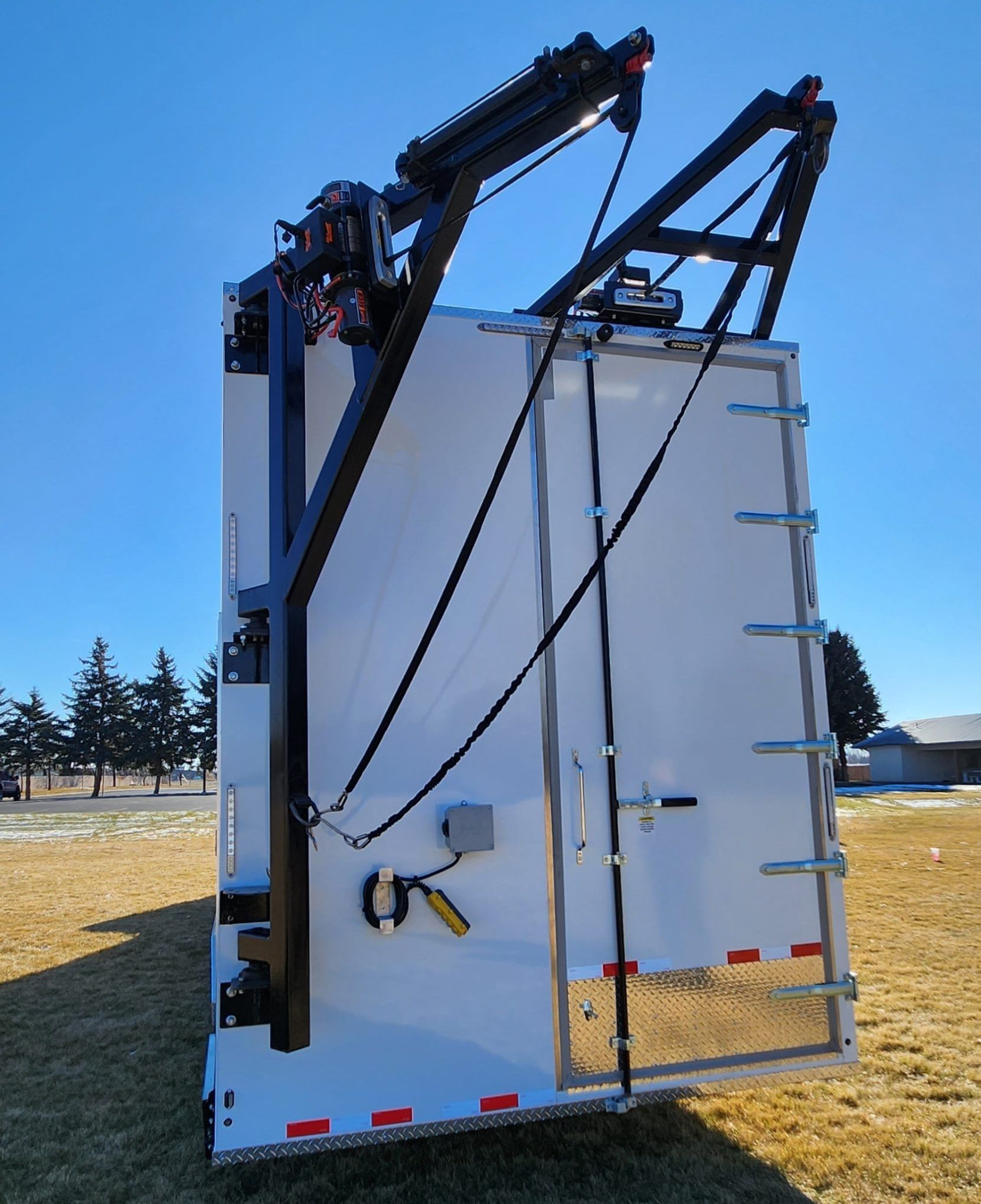 Rear view of a white utility truck body with raised black lift arms outdoors on a grassy field.