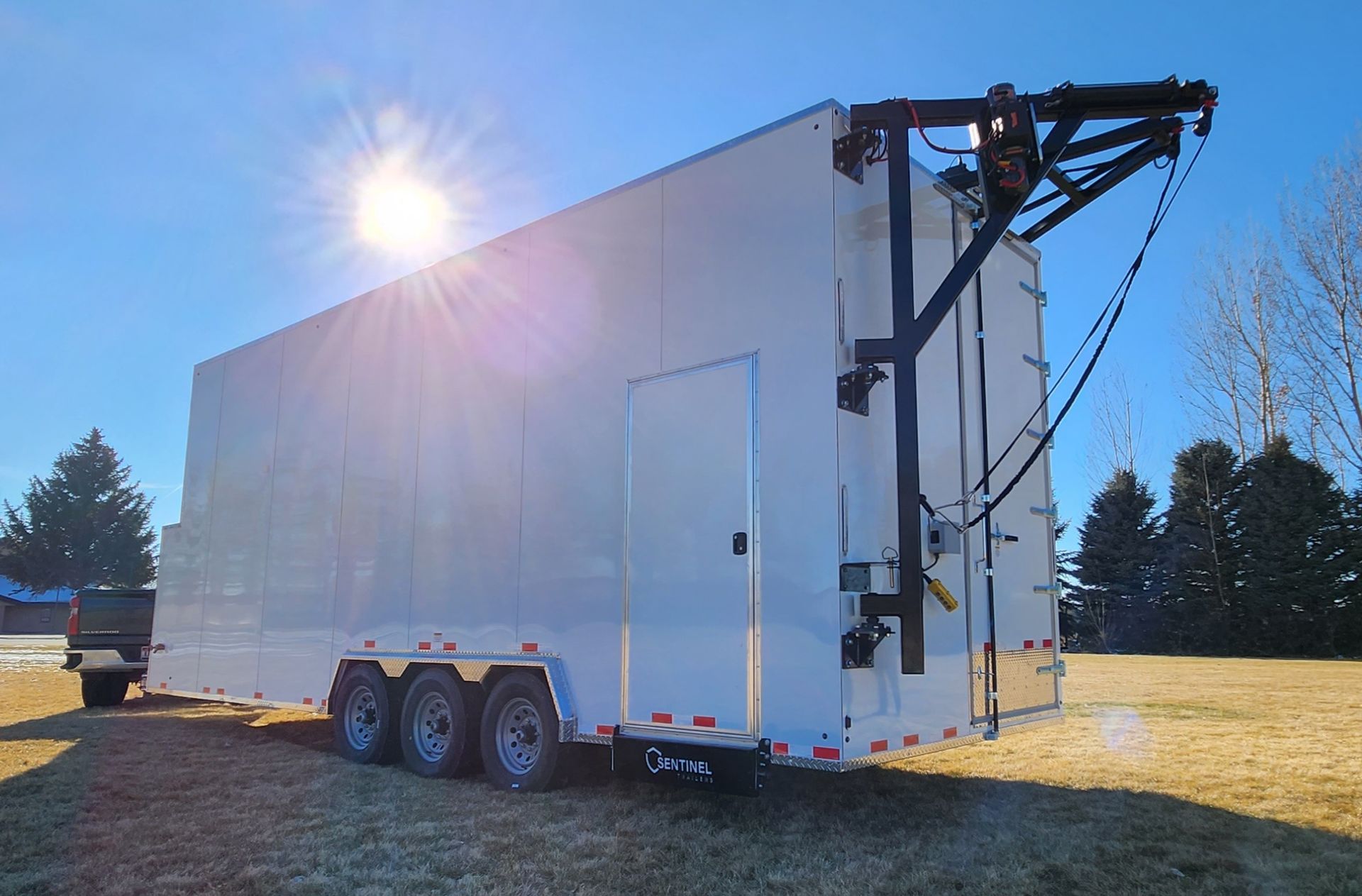 White enclosed trailer with triple axles parked on grass in bright sunlight, side ramp deployed.