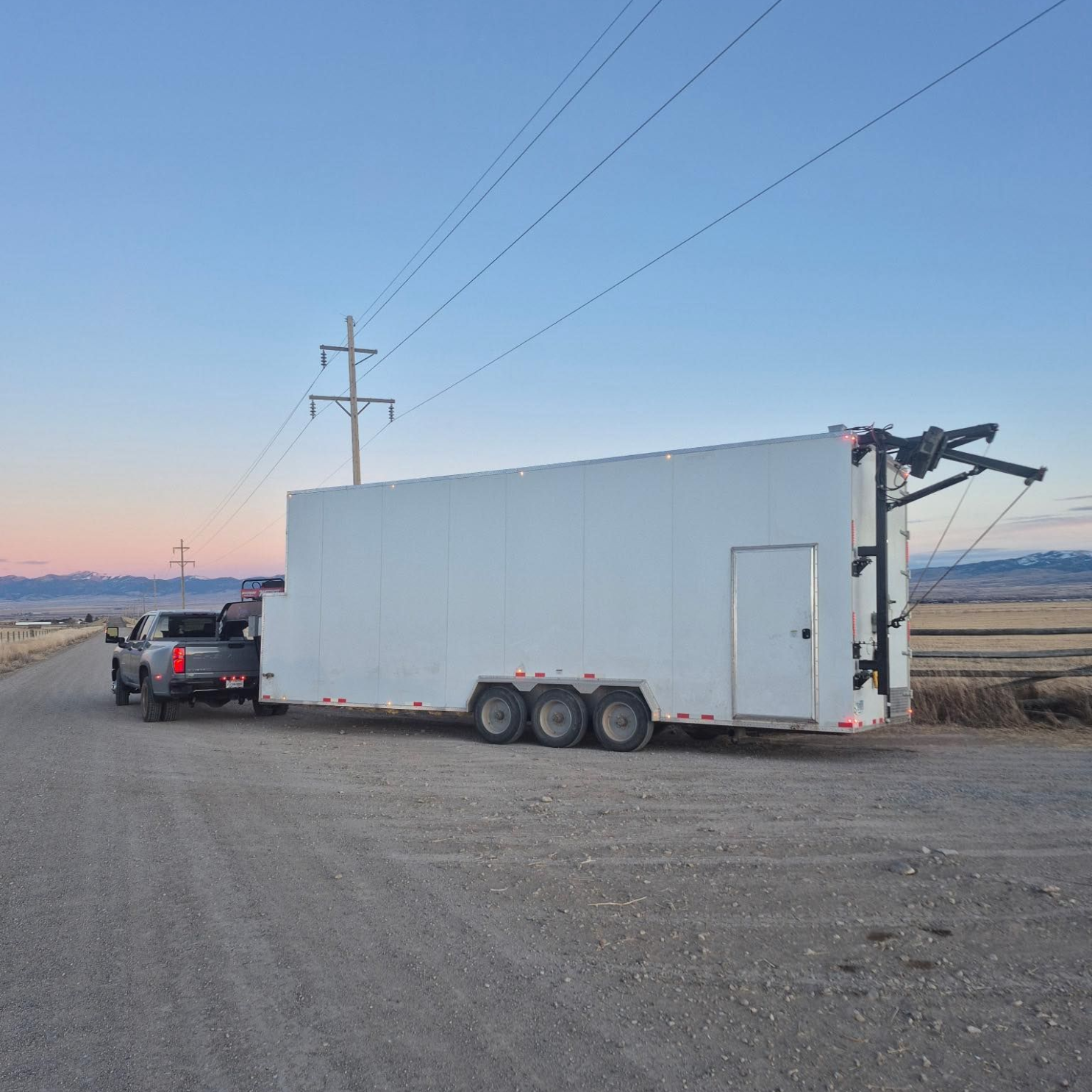 White cargo Sentinel trailer with side-mounted AC unit parked on a gravel lot beside a pickup truck.
