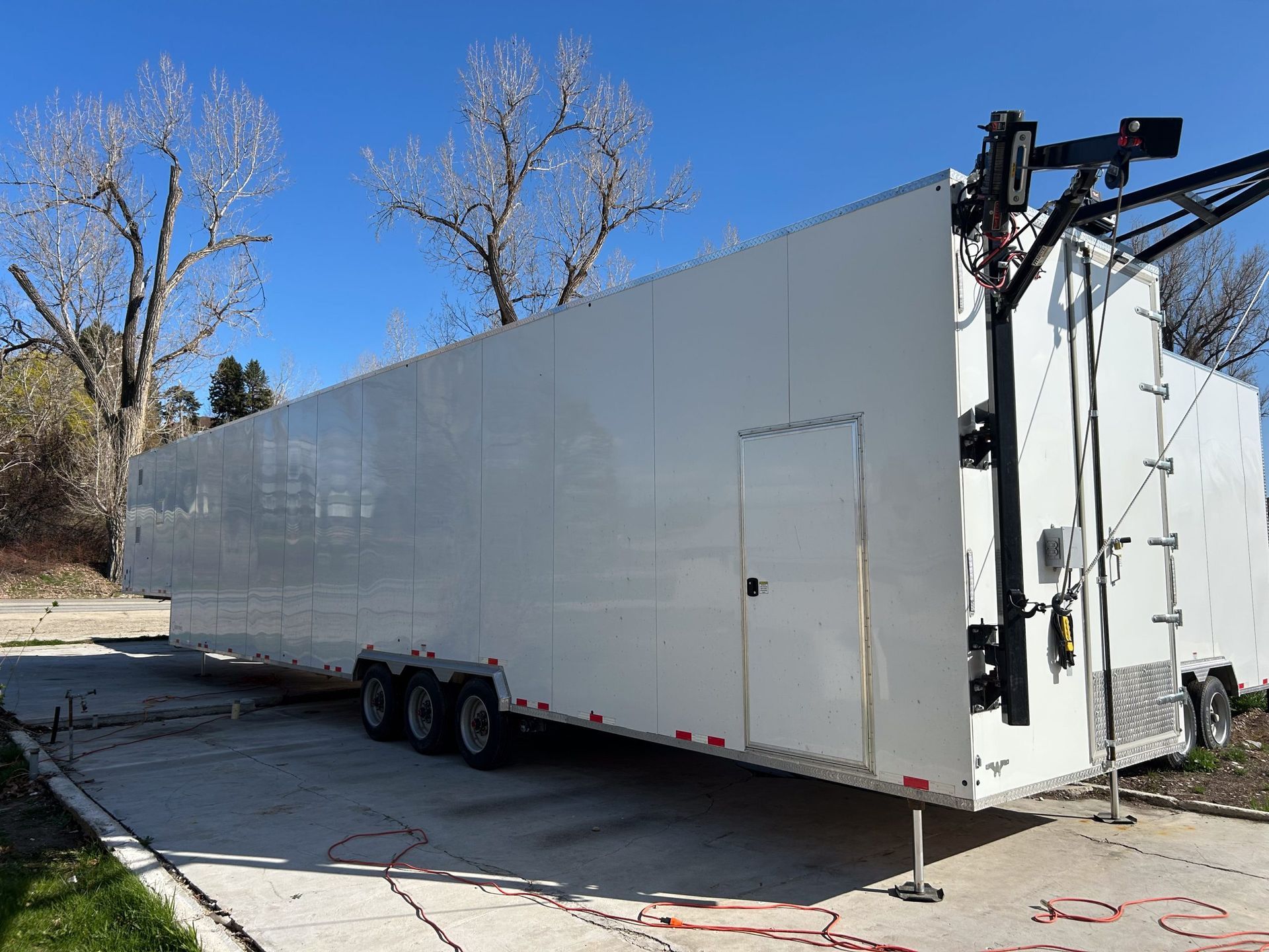 White enclosed semi-trailer parked outdoors on a sunny road, with trees and clear blue sky.