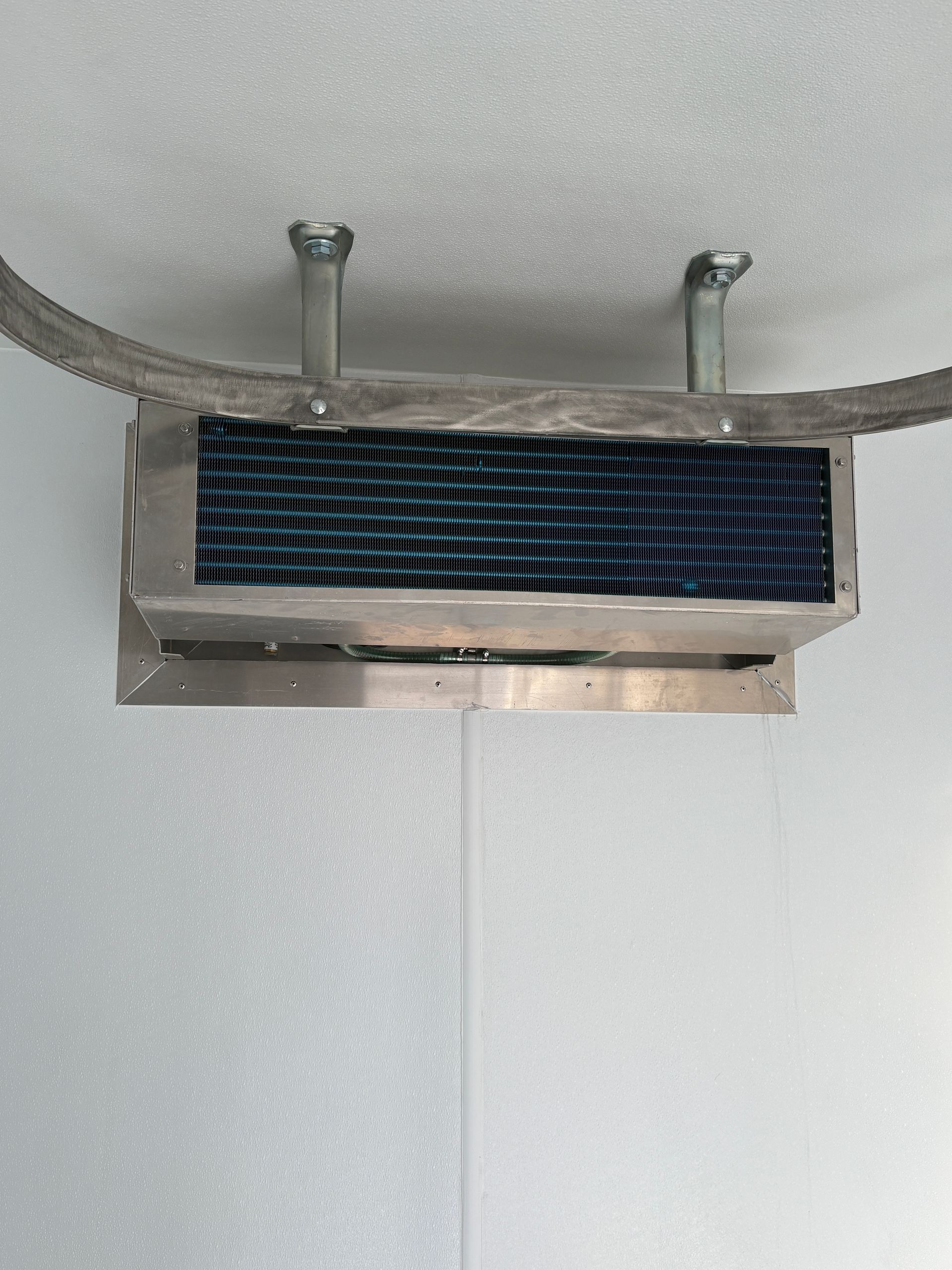 Wall-mounted rectangular vent with a blue mesh filter beneath a curved ceiling.