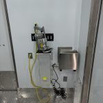 Wall-mounted meat processing equipment with cords and a stainless-steel dispenser in a clinical hallway