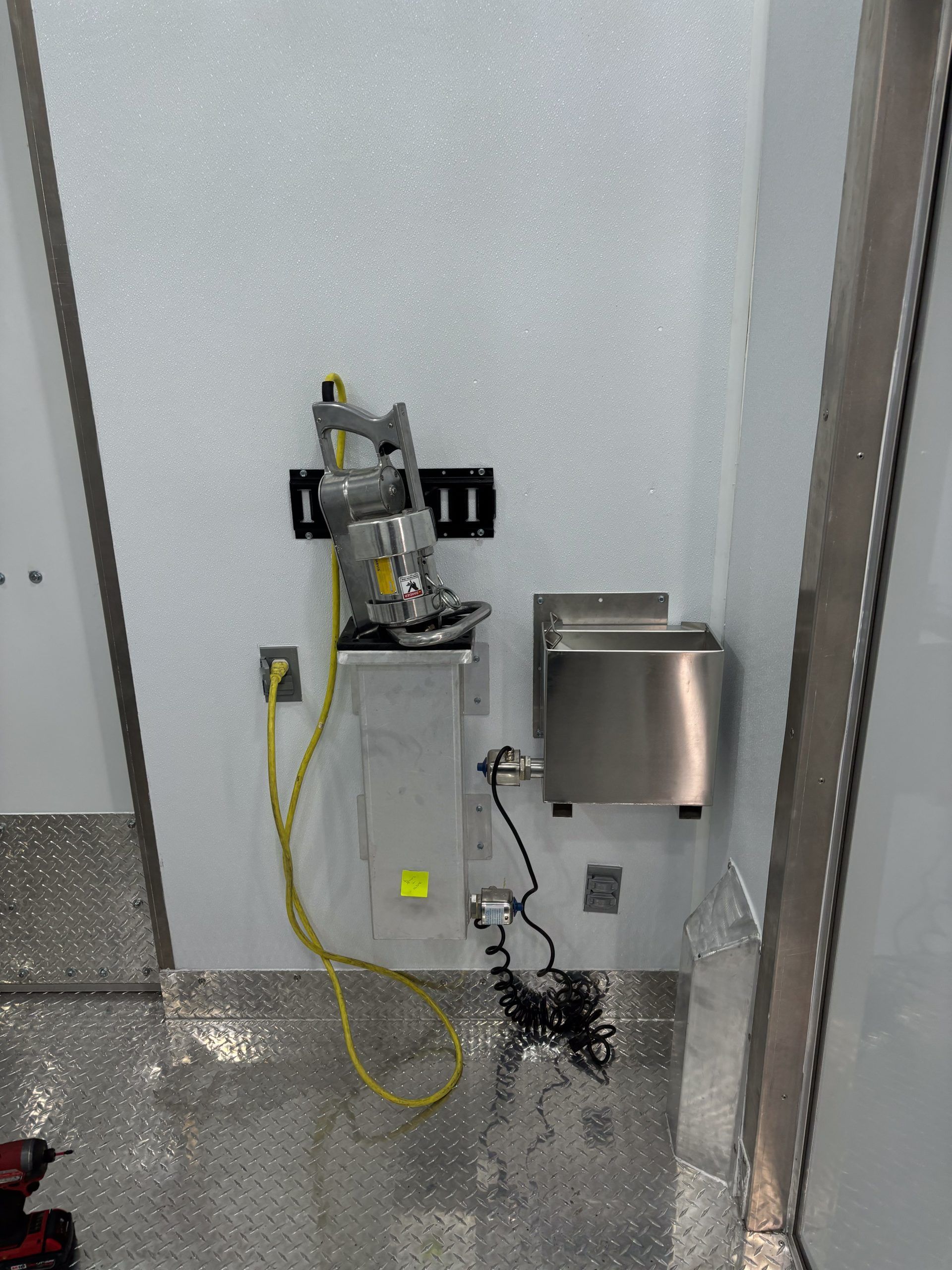 Wall-mounted industrial control panel with a hose, cables, and a stainless steel dispenser in a utility room