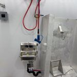Wall-mounted stainless steel sink with red and blue hoses in a butcher trailer