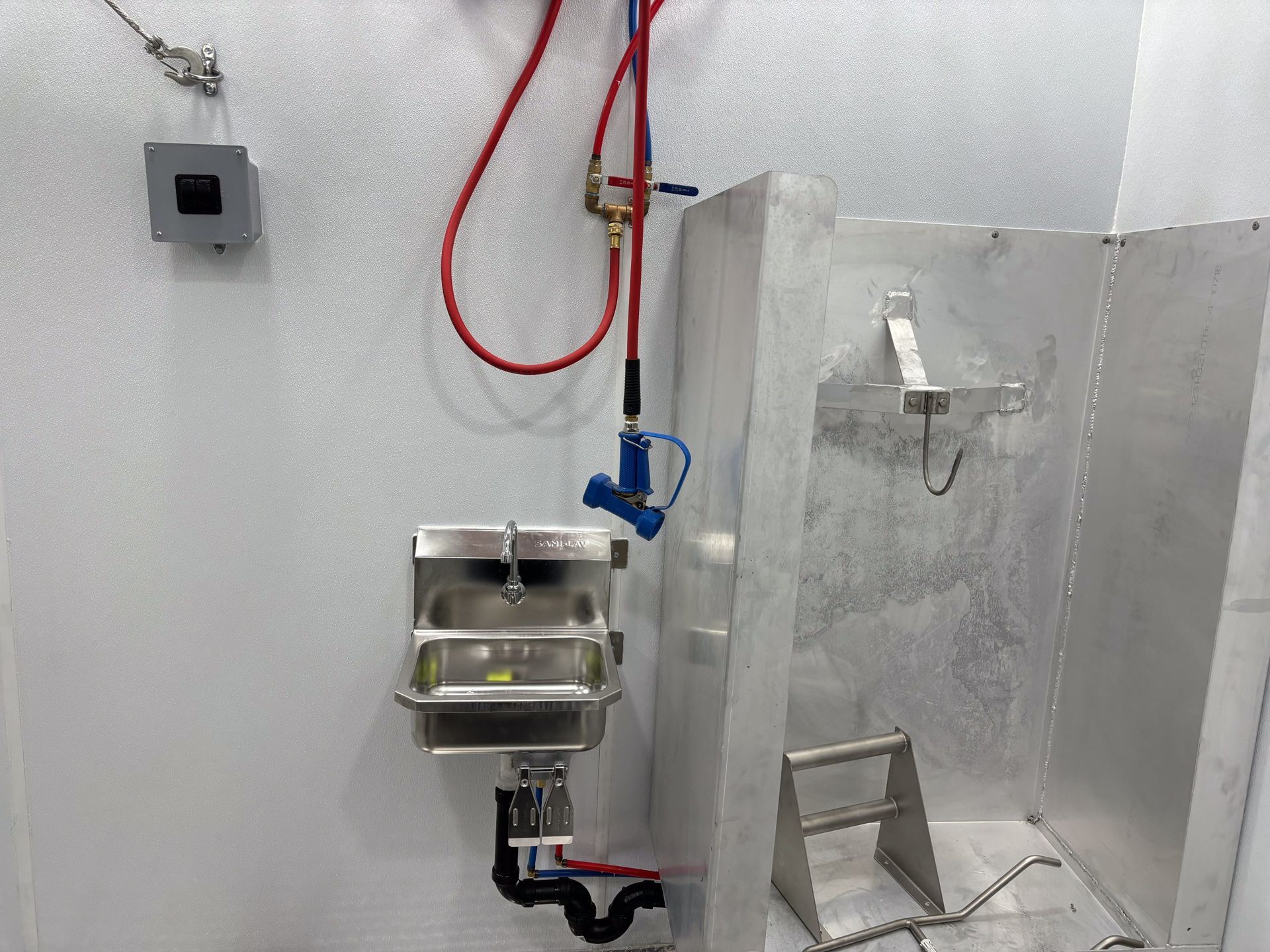 Stainless steel sink and shower area in a small utility room with wall-mounted hoses and fixtures
