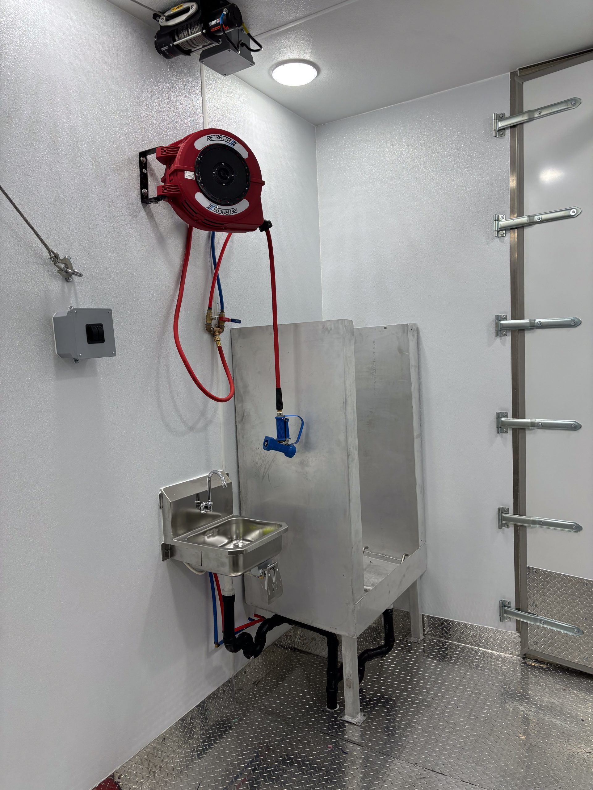 Industrial stainless steel with wall-mounted hose, sink, and safety chair.