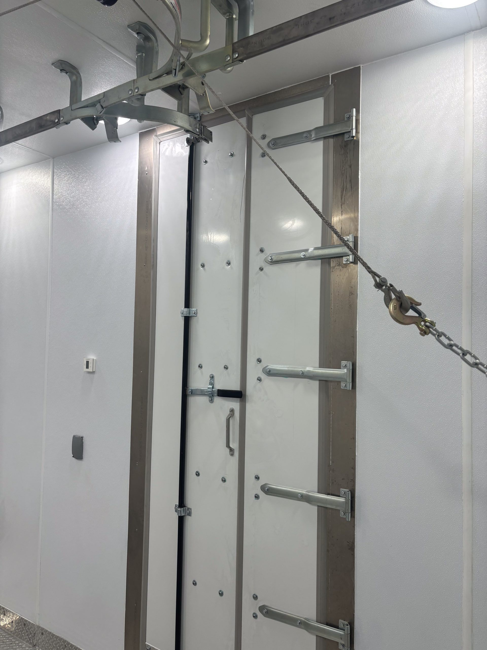 Industrial ladder inside a white metal room, with rails, brackets, and a hanging chain on the right.