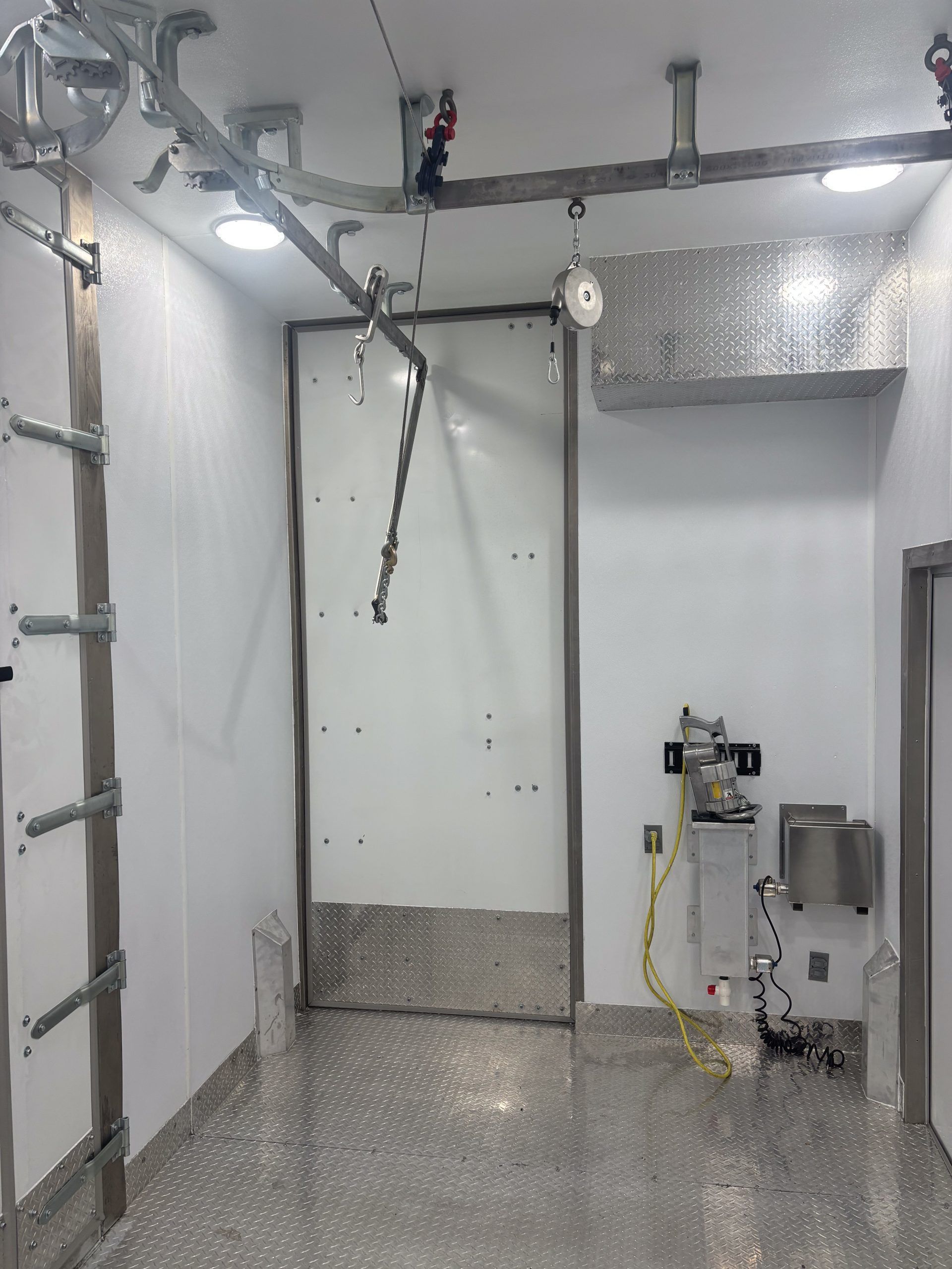 Empty industrial room with diamond-plate floor, overhead rails, and a wall-mounted sink.