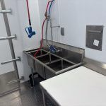 Stainless-steel hospital sink with blue faucet and countertop in a meat processing trailer