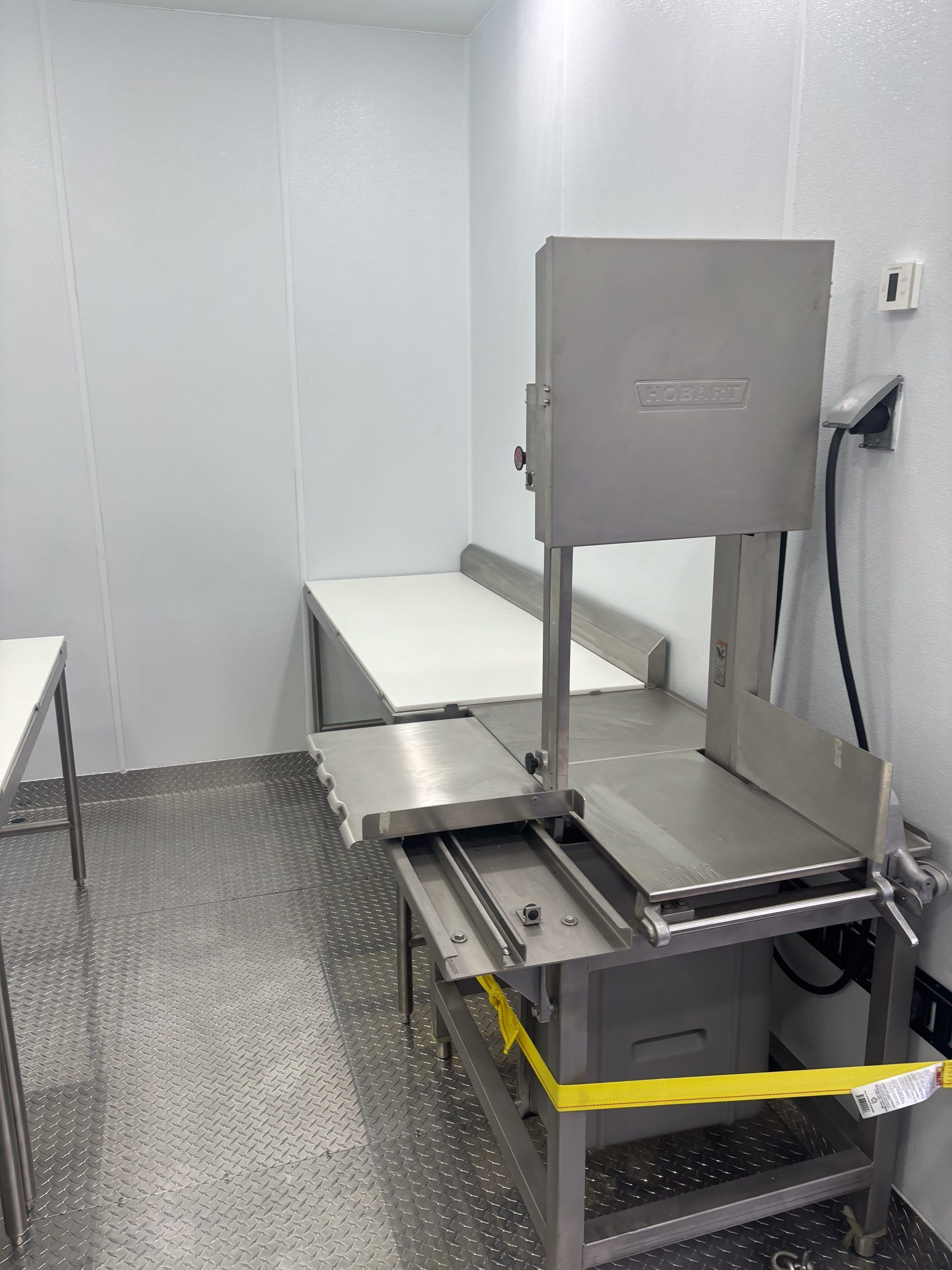 Industrial metal machine in a white room, with a yellow safety strap across the front.